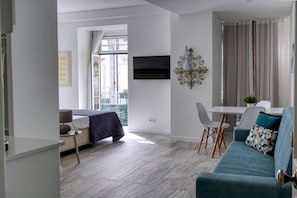 A modern living room with a bed, a TV mounted on the wall, a dining area with a table and chairs, and a balcony with a view. - PB SUP Ria Formosa - Palacete da Baixa (Faro)