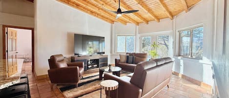 A spacious living room with a wooden ceiling, a flat-screen TV, leather sofas, and a dining area with a table and chairs.