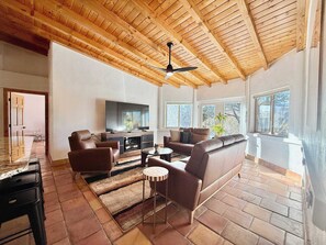 Un salon spacieux doté d’un plafond en bois, d’un téléviseur à écran plat, de canapés en cuir et d’un coin repas avec une table et des chaises.