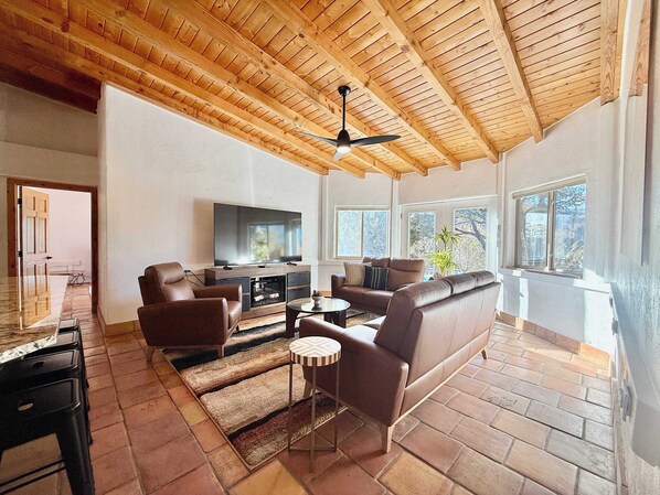 A spacious living room with a wooden ceiling, a flat-screen TV, leather sofas, and a dining area with a table and chairs.