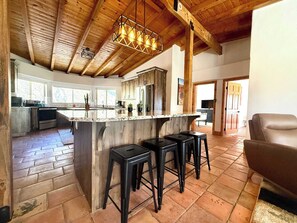 A spacious kitchen with a large island, bar stools, and a wooden ceiling.