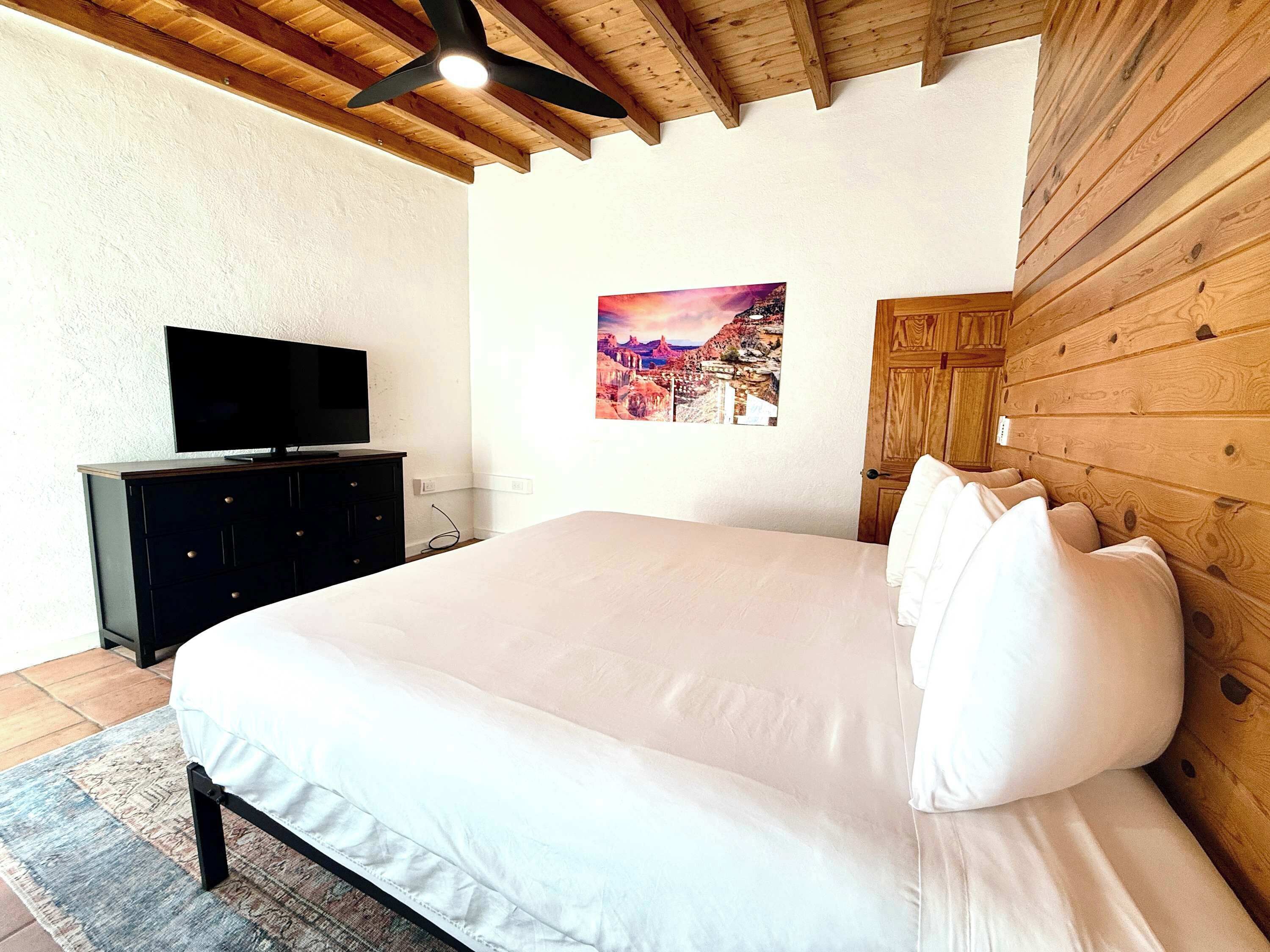 Une chambre à coucher avec un lit, un téléviseur posé sur une commode et un plafond en bois.