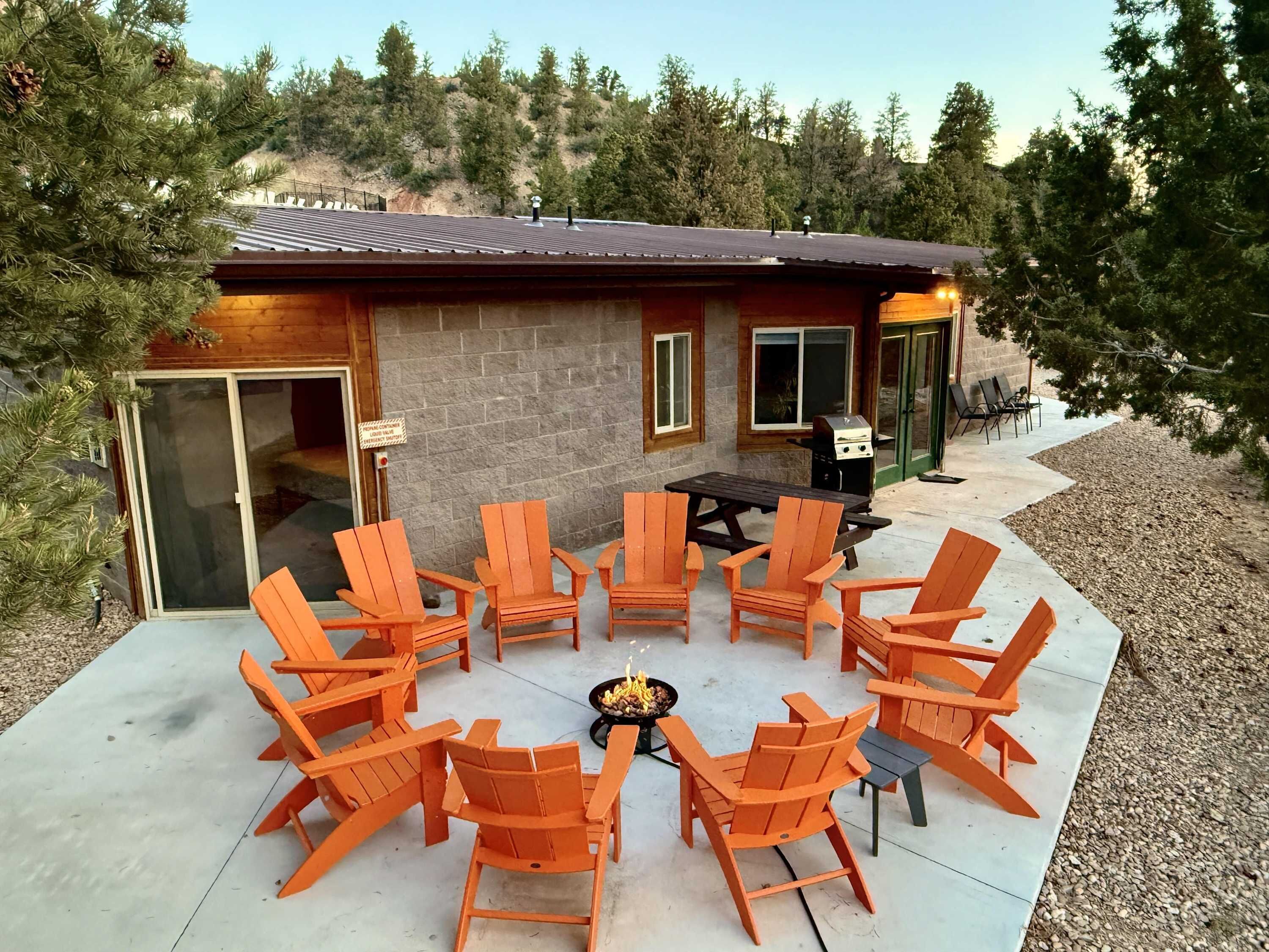 An outdoor patio with wooden chairs and a table, a barbecue grill, and a stone building with a tiled roof.