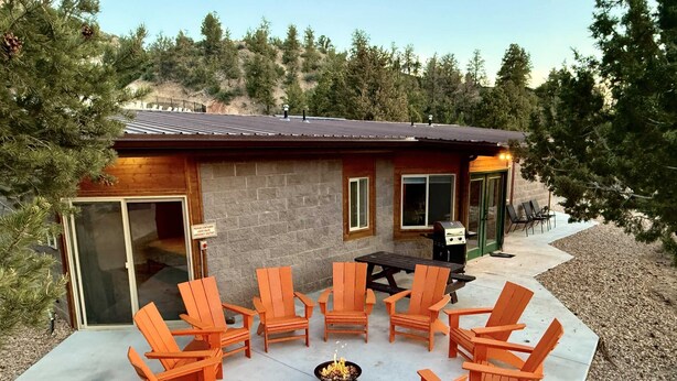 Eine Terrasse im Freien mit Holzstühlen und einem Tisch, einem Grill und einem Gebäude mit Ziegeldach.