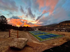 A tennis court with a wooden fence and a large rock nearby.