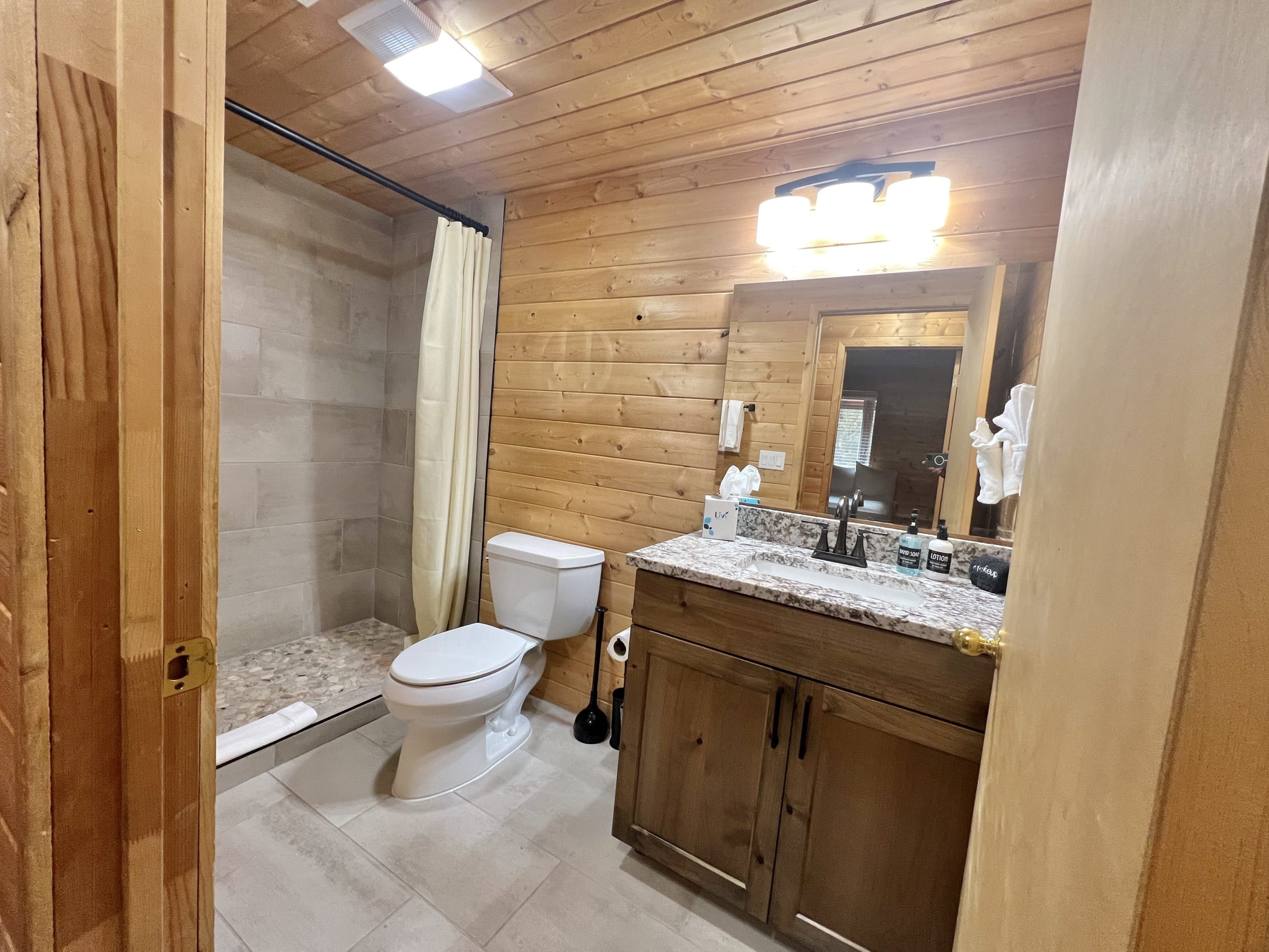 A wooden-paneled bathroom with a toilet, sink, and shower.