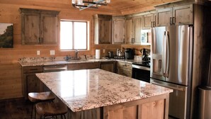 A kitchen with wooden cabinets, a granite countertop, stainless steel appliances, and a large island with bar stools.