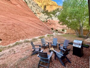 Zona salotto all'aperto con poltrone Adirondack e un barbecue, con sullo sfondo formazioni rocciose rosse e un albero.