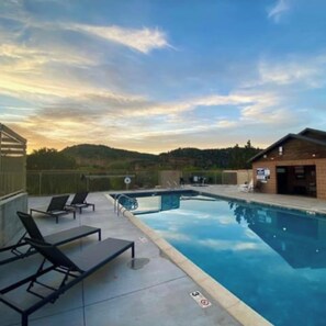 A swimming pool with lounge chairs, a small building, and a scenic view of hills.