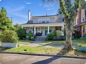 A two-story house with a porch, steps leading to the entrance, and a garden with a tree and plants. - Calm and Private Room in NE Portland (Portland)