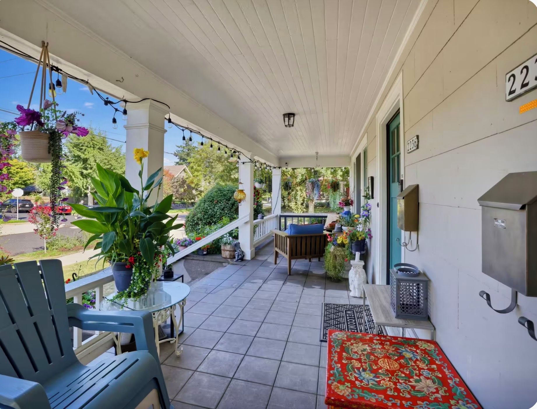 A covered porch with a bench, a table, and hanging flower baskets.