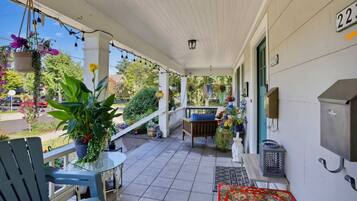 A covered porch with a bench, a table, and hanging flower baskets.