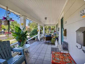 Une véranda avec un banc, une table et des jardinières suspendues.