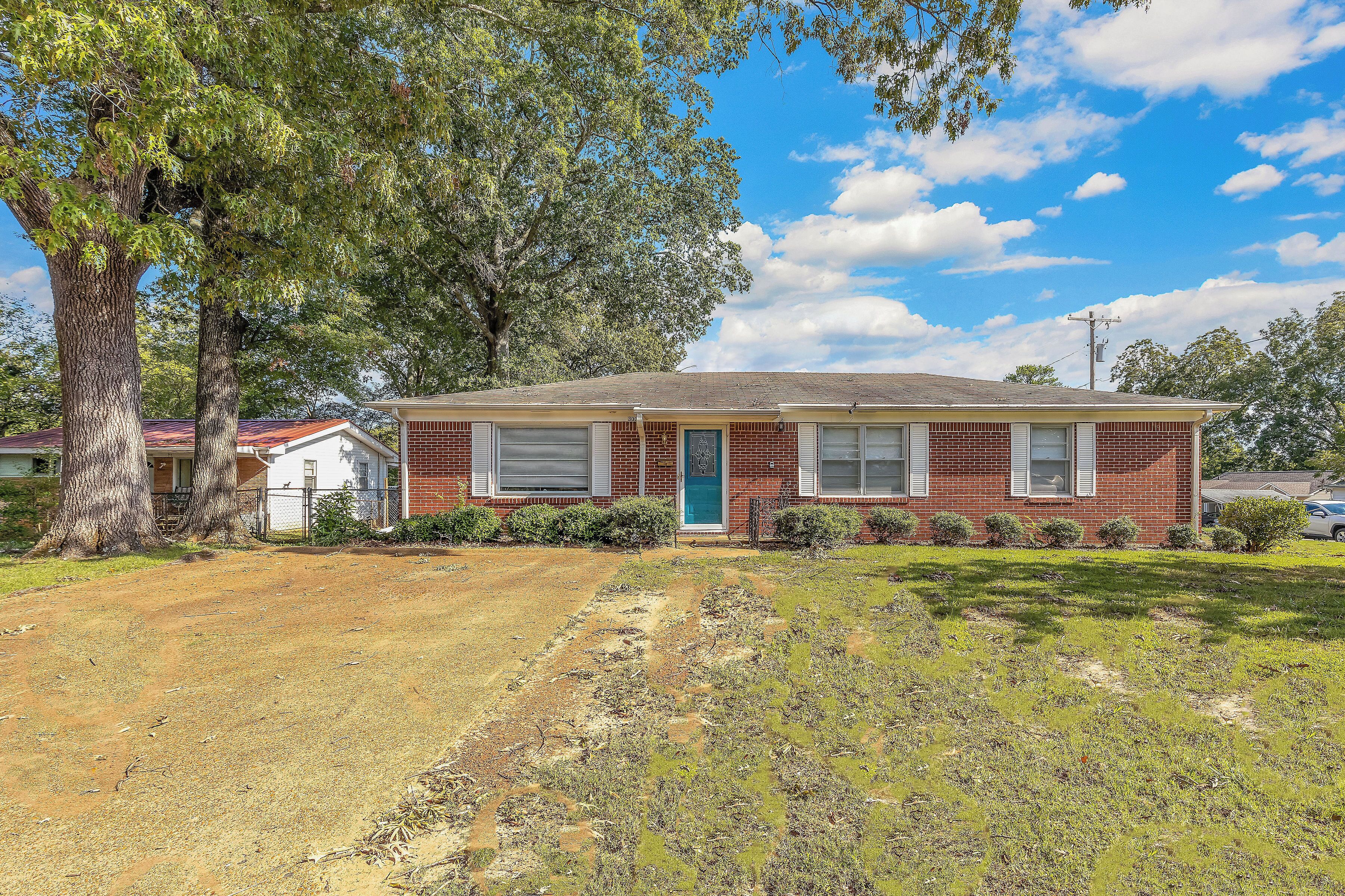 A single-story brick house with a front yard, a blue door, and a small front porch.