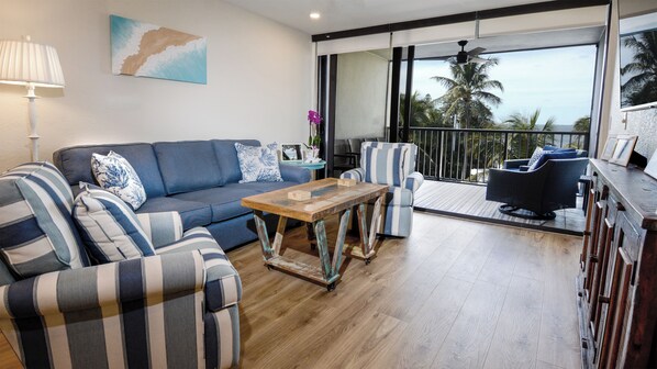 A modern living room with a sofa, striped armchairs, a coffee table, and a balcony with outdoor furniture.