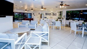 Un restaurant avec des meubles blancs, des ventilateurs de plafond et une enseigne au mur indiquant « MOON BAY ».