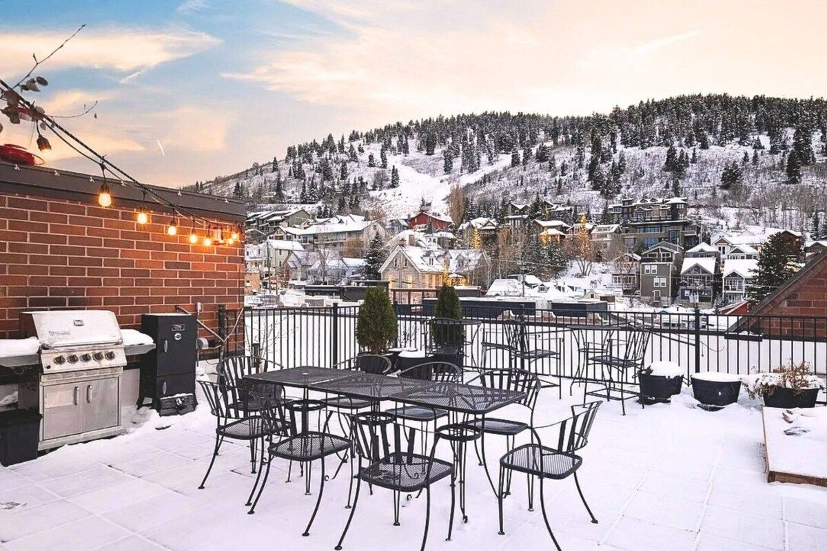 Eine Terrasse mit Gartenmöbeln und Grill, mit Blick auf eine verschneite Stadt und Hügel.