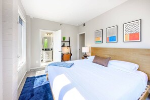 A hotel room with a large bed, a wooden headboard, a blue rug, and artwork on the wall.