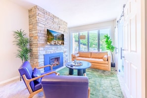A living room with a stone fireplace, leather furniture, and a large window offering a view of greenery.