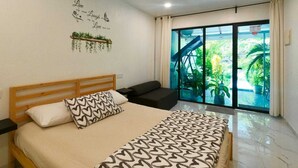 Une chambre à coucher comprenant un lit, un ventilateur de plafond, une fenêtre donnant sur un paysage verdoyant et un mur orné d’une inscription décorative.