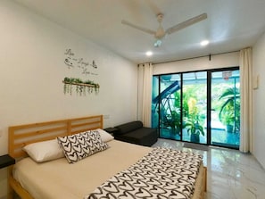 A bedroom with a bed, a ceiling fan, a window with a view of greenery, and a wall with a decorative phrase. - Oceana Inn Maldives (Kudahuvadhoo)