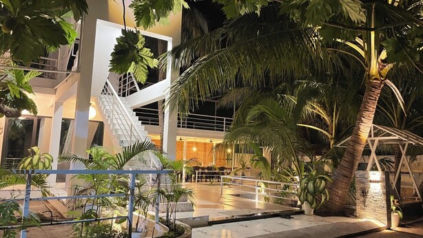 A modern building with a staircase, palm trees, and a well-lit entrance area. - Oceana Inn Maldives (Kudahuvadhoo)