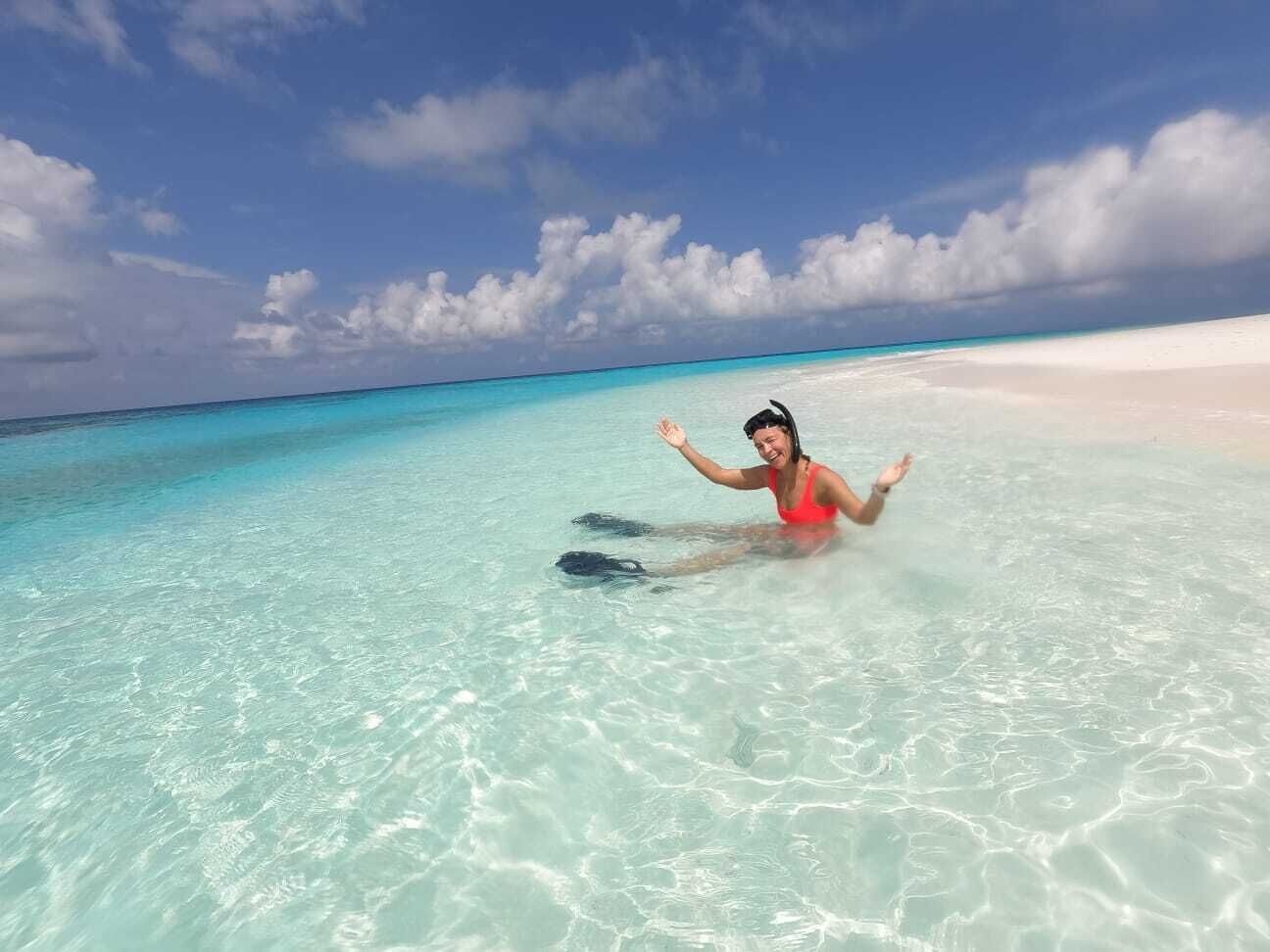 Una persona con traje de baño rojo en aguas turquesas cristalinas, con una playa de arena blanca y un cielo despejado.