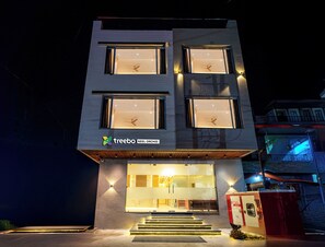 A modern building with multiple illuminated windows and a visible entrance with steps leading up to it. - Treebo Neel Orchid (Ujjain)