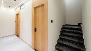 Ein moderner Flur mit einer Holztür, einer Treppe mit schwarzen Stufen und Einbauleuchten an der Decke.