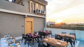 Eine Dachterrasse mit Tischen und Stühlen, Klimaanlagen und Blick auf den Sonnenuntergang.