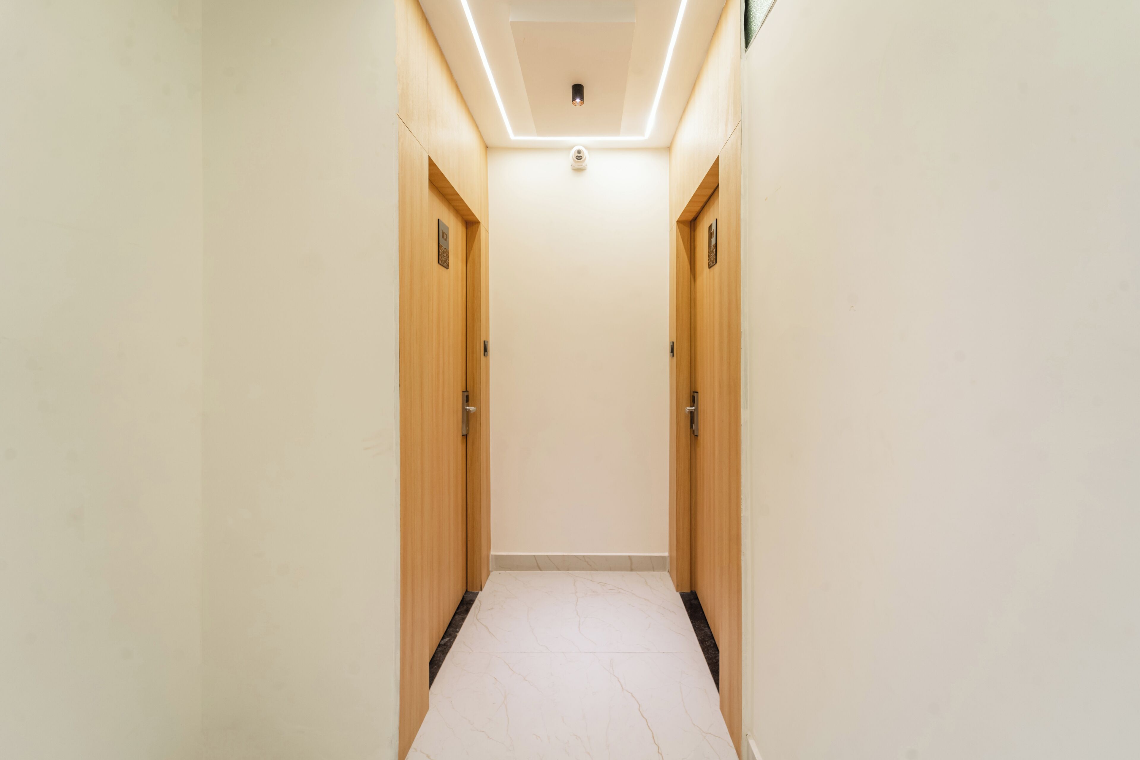 A narrow hallway with wooden doors on either side, a tiled floor, and a ceiling light fixture.