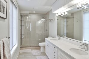 Enjoy a refreshing shower in the walk-in shower with glass doors, a separate toilet, and a vanity with a large mirror.