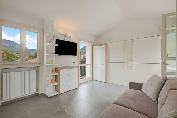 A modern living room with a sofa, TV, white cabinets, and a view of mountains.