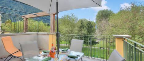 A balcony with a table set for two, outdoor furniture, and a view of a park and mountains.