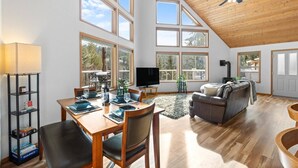 A spacious living area with a high ceiling, large windows, a fireplace, and a cozy seating area. - Cave Bay Escape - Stunning CDA Lake View, Deck, Grill, Blackstone, Fire Pit, and near Boat Launch! (Worley)