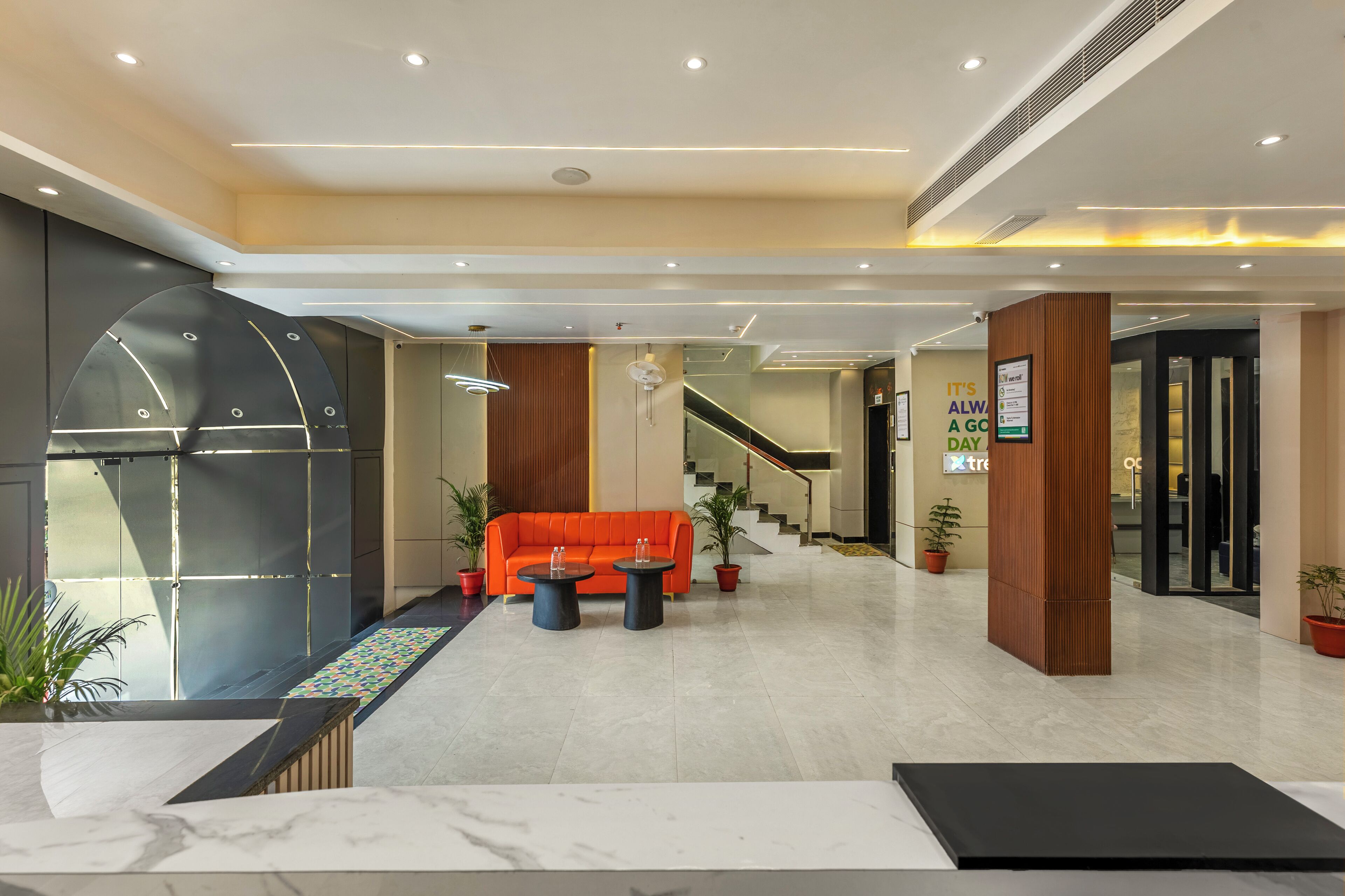 Un hall d’entrée moderne avec un comptoir d’accueil, un canapé orange vif et un escalier menant aux étages supérieurs.