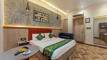 A modern hotel room with a large bed, a desk with a laptop, a small table with a cup and a plate of food, and a large mirror.
