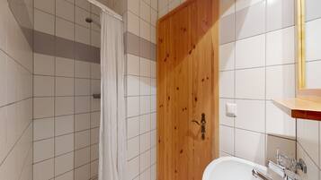 A bathroom with a shower, a wooden door, a white sink, and a mirror.