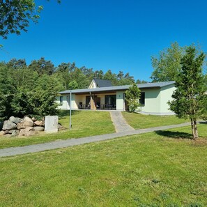 A two-story house with a front porch, a stone wall, and a paved driveway.
