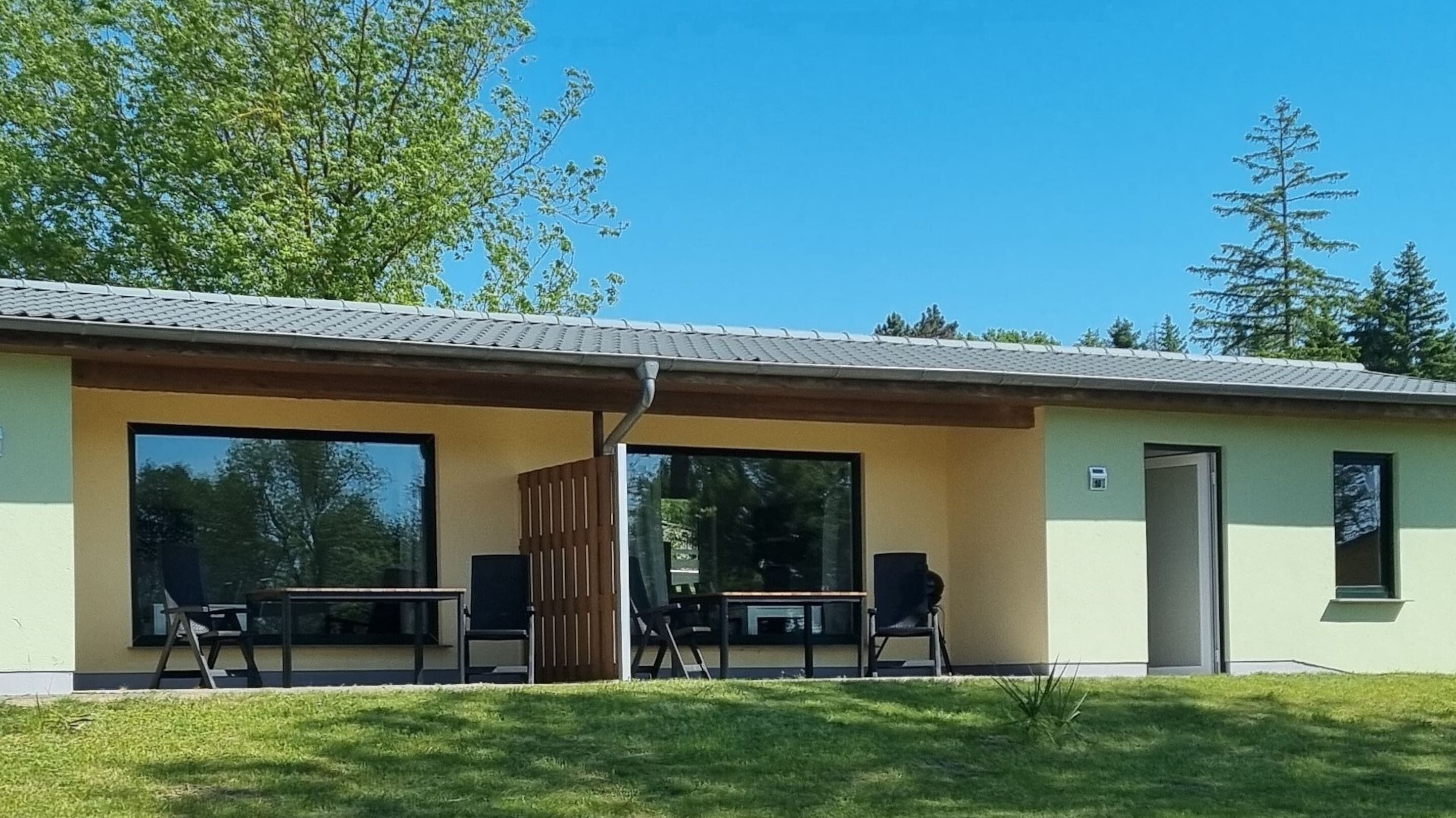 A modern building with a covered patio area featuring two tables and chairs, large windows, and a door.