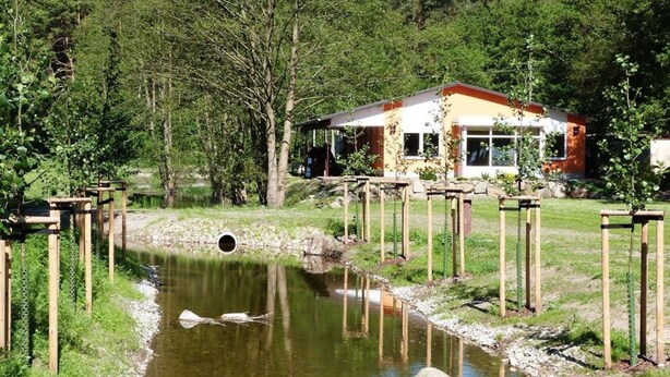 A riverside building with a covered outdoor area, surrounded by greenery and trees. - Reihenhaus am Gross Labenzer See, Klein Labenz (Warin)
