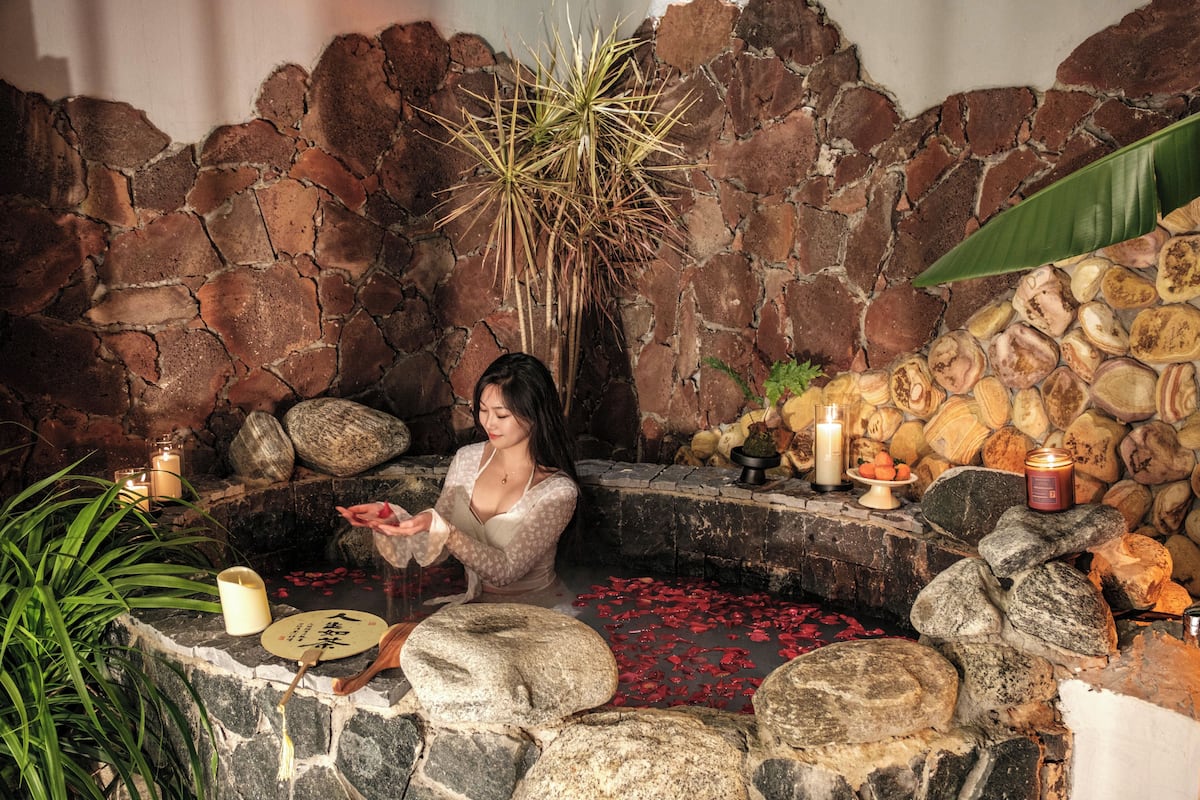 A stone bath area with candles, a plant, and a stone wall.