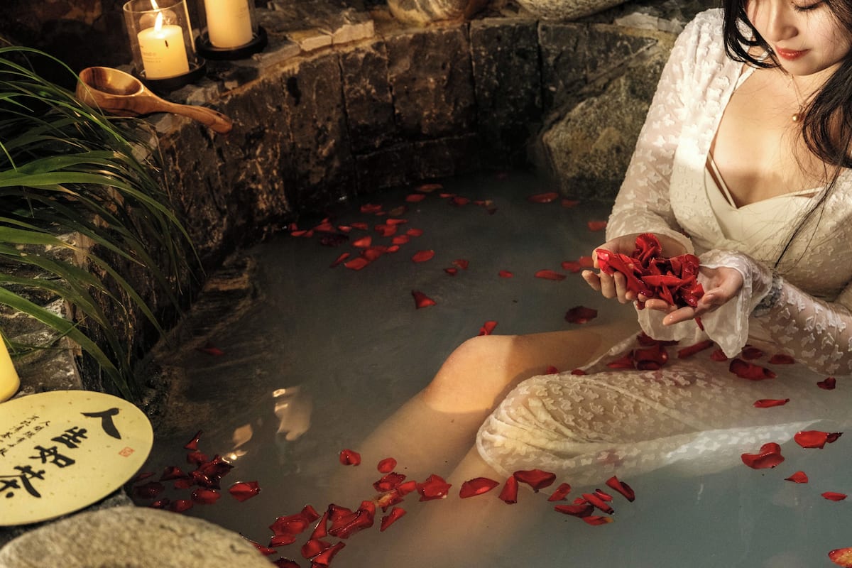 A person in a stone bath surrounded by rose petals and candles.