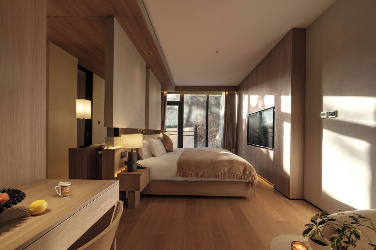 A modern hotel room with a large bed, a desk with a lamp, a coffee cup, and a plant.