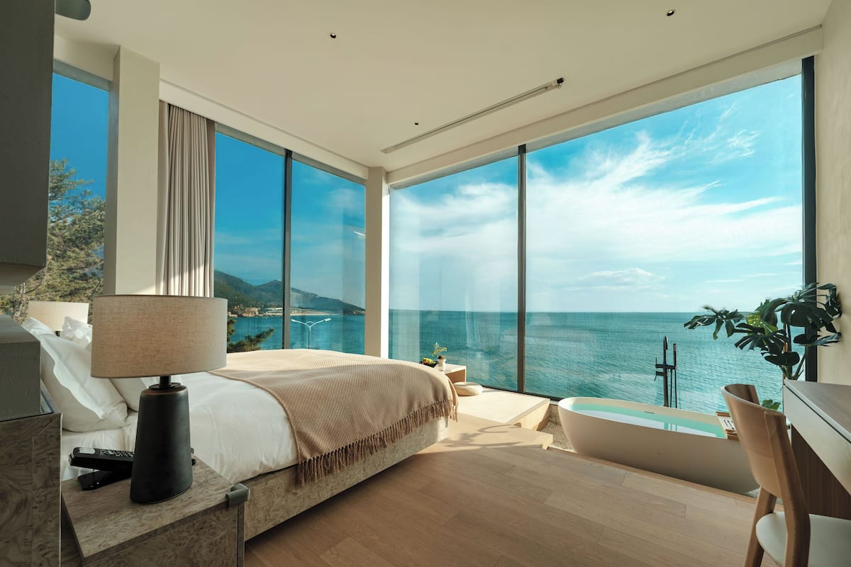 A modern bedroom with a large bed, a bathtub, and a view of the sea.