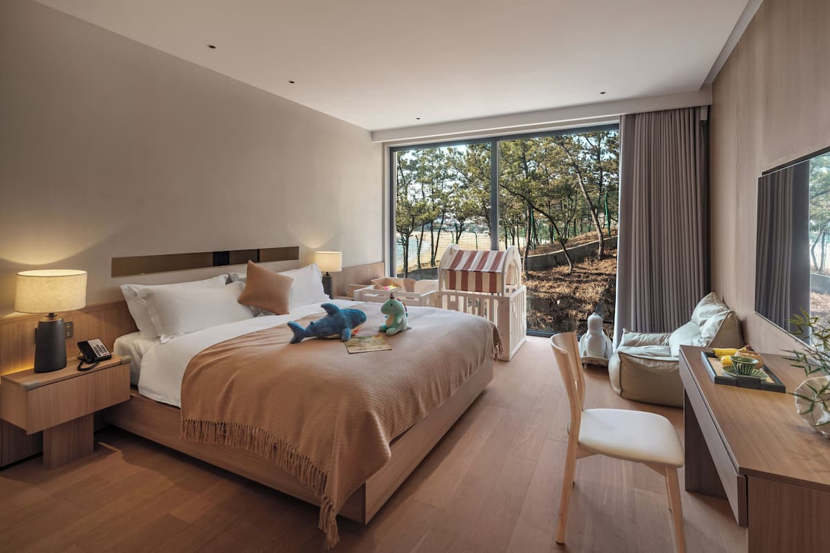 A modern hotel room with a large bed, bedside tables, a desk, and a view of the outdoors.