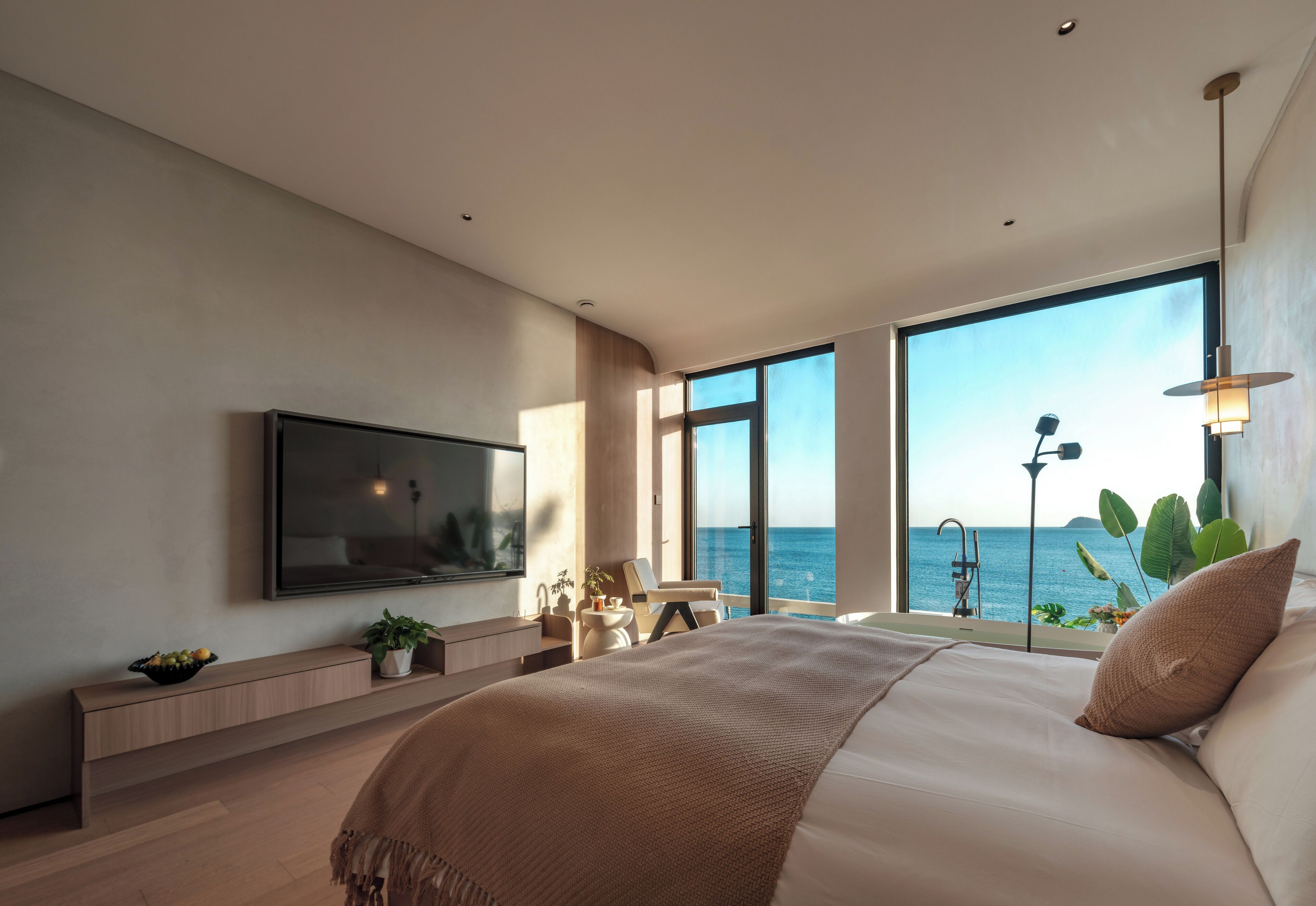 Un dormitorio moderno con una cama grande, un televisor montado en la pared y vistas al mar.