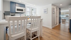 Una cocina moderna con armarios blancos, microondas y comedor con sillas blancas.