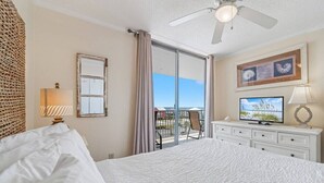 A hotel room with a bed, a television, a ceiling fan, a window with curtains, and a view of the outdoors. - 2BR Boat Friendly Condo Updated Pool Beach Access (Gulf Shores)