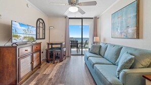 A living room with a sofa, a TV, a ceiling fan, and a painting on the wall. - 2BR Boat Friendly Condo Updated Pool Beach Access (Gulf Shores)